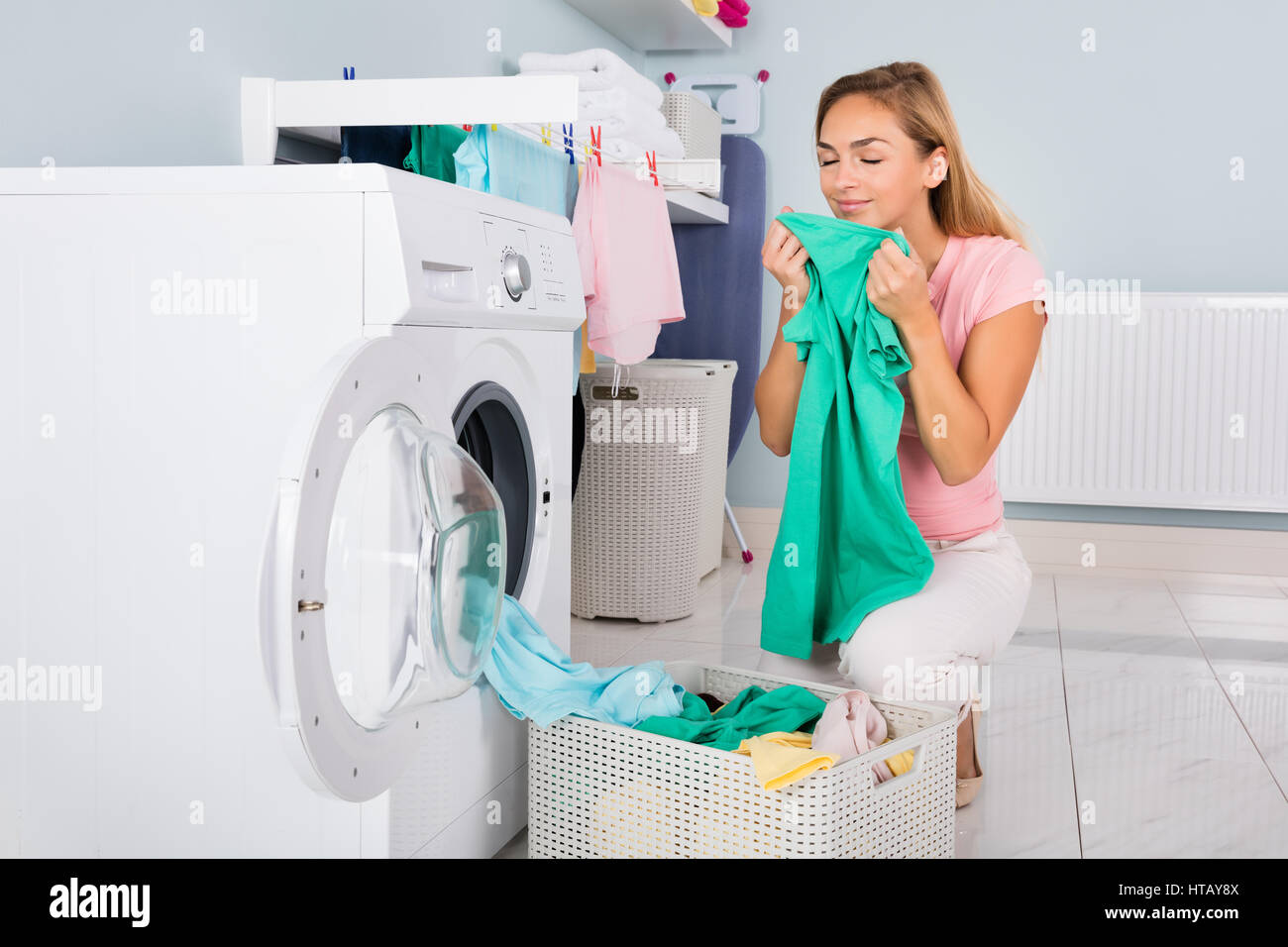 Junge lächelnde Frau riecht Kleidung nach dem Waschen In der Waschmaschine im Hauswirtschaftsraum Stockfoto