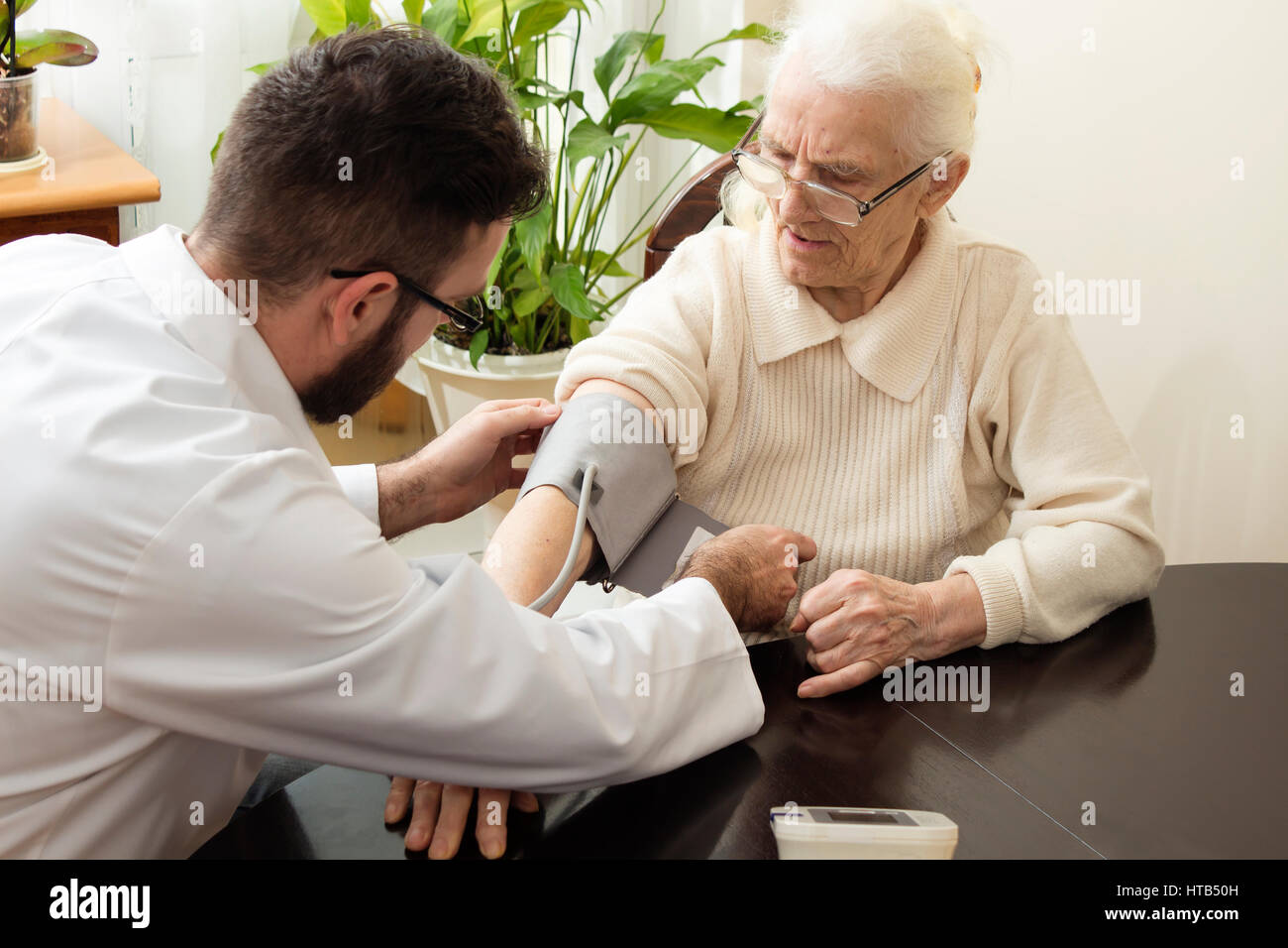 Eine private Arztpraxis. Geriater Arzt nimmt den Patienten und ihren Blutdruck messen. Stockfoto