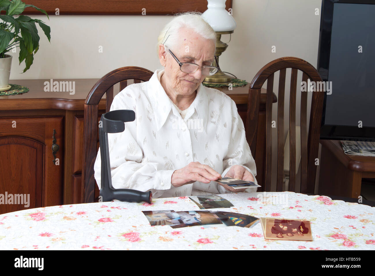 Alte Frau sitzt im Wohnzimmer am Tisch und schaut alte Fotografien. Alte Großmutter beobachten alte Fotos, die am Tisch sitzen. Stockfoto