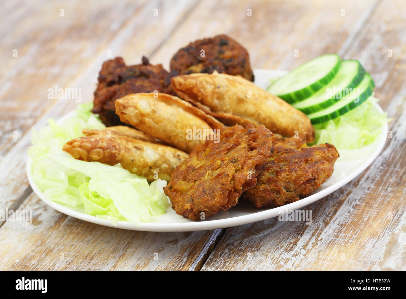 Indische Snacks wie Zwiebel-Bhajis, Samosas und Pakoras auf weißen Teller auf Holzuntergrund Stockfoto