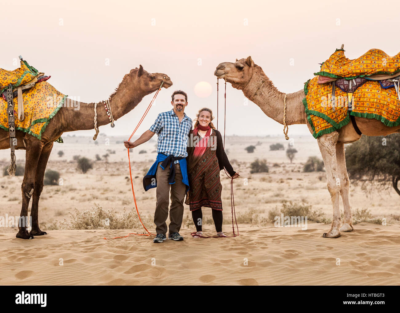 Ein Mann und eine Frau hält ihre Kamele herrscht beim posieren für ein Foto in der Thar-Wüste bei Sonnenuntergang, Rajasthan, Indien. Stockfoto