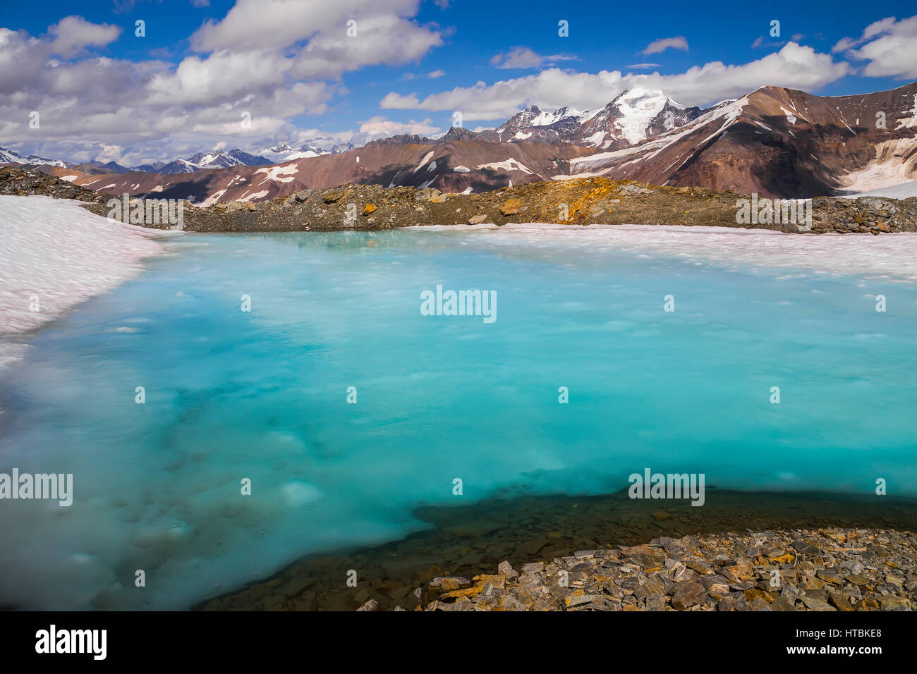 Eine Lache des Wassers liegt an einem Schnee-Patch hoch auf einem Bergrücken im Bereich von Alaska im Sommer.  Der Berg im Hintergrund ist White Princess Stockfoto