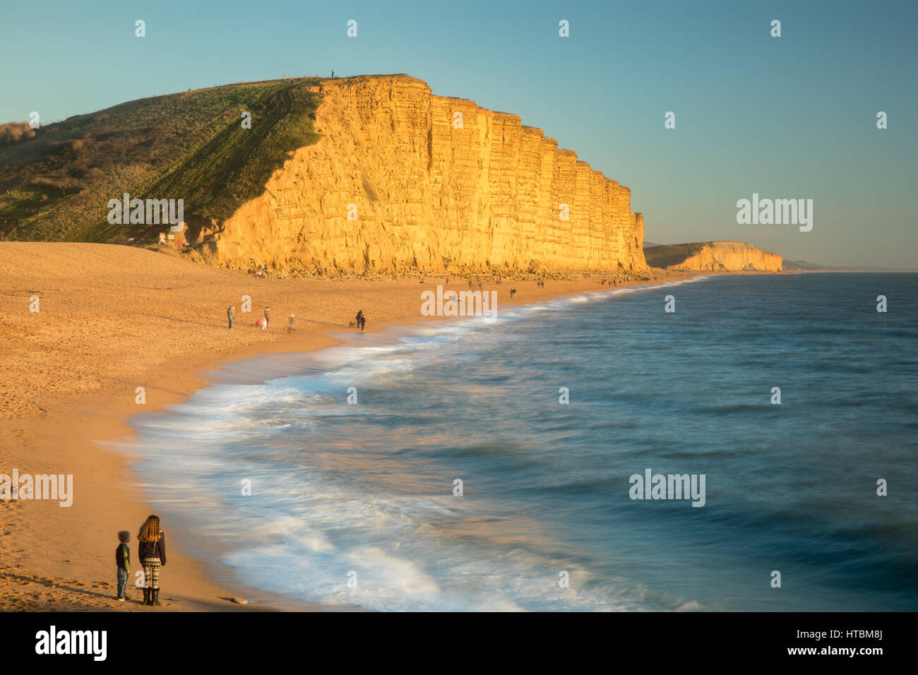 Bruder und Schwester, die gerade Wellen brechen am Strand unterhalb East Cliff, West Bay, Jurassic Coast, Dorset, England, UK Stockfoto