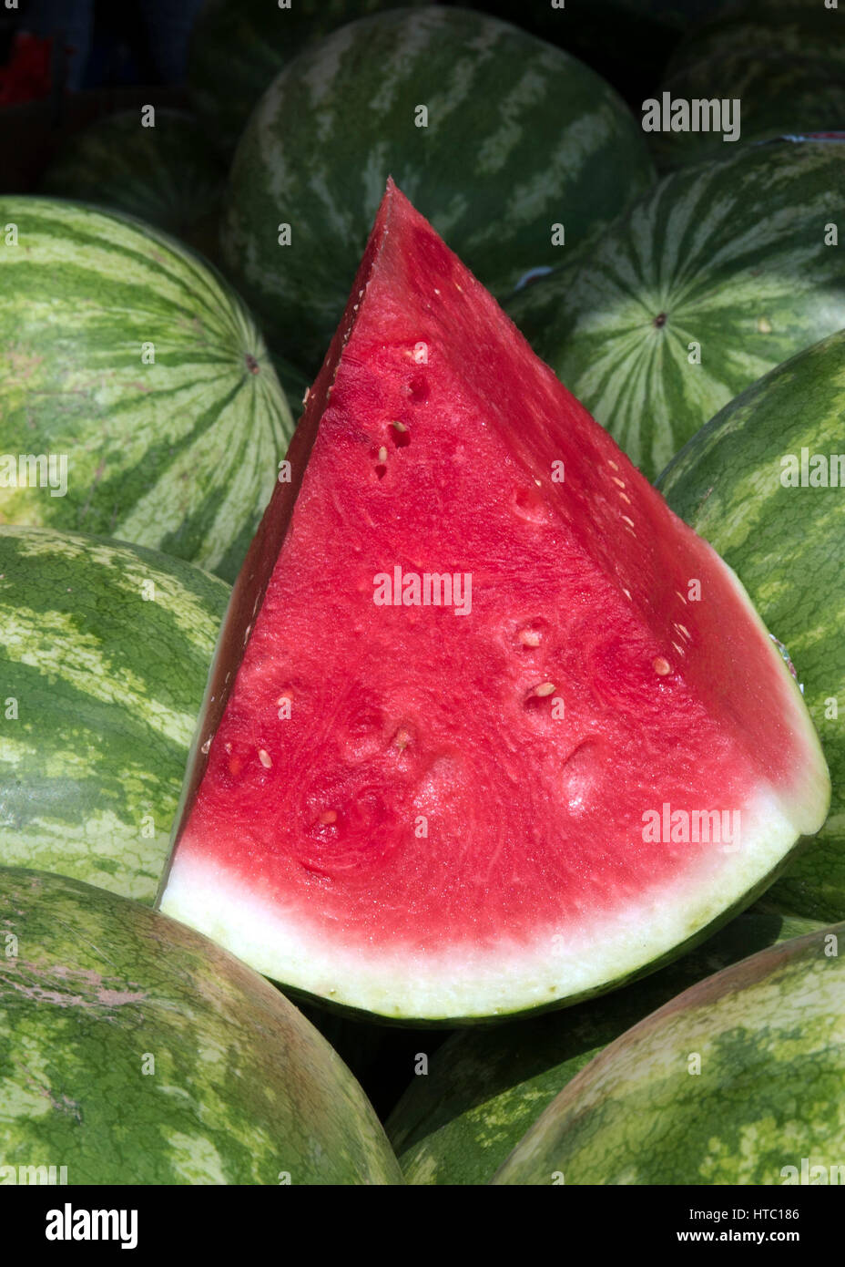 Vertikaler Schnitt rote Wassermelone sitting on Top of mehrere Melonen am Markt. Stockfoto