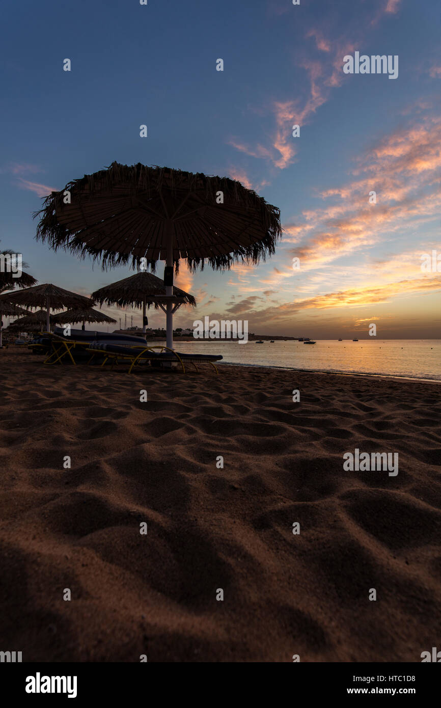 Bunte Wolken über den Strand bei Sonnenaufgang mit strohgedeckten Sonnenschirmen in der silhouette Stockfoto