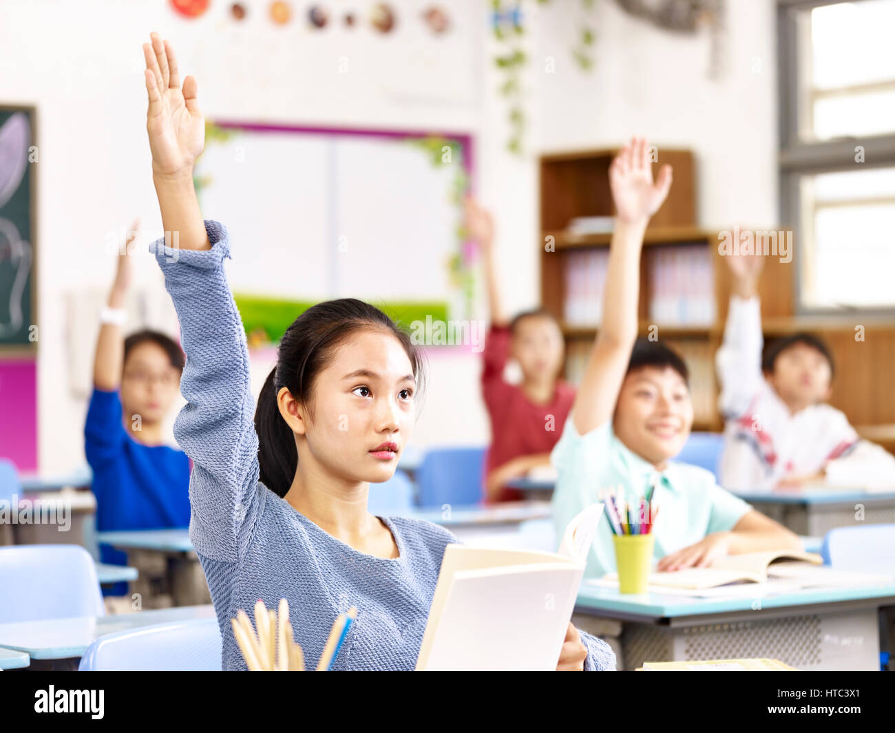 asiatische Grundschule jungen Hände erhebend für Fragen während des Unterrichts im Klassenzimmer. Stockfoto