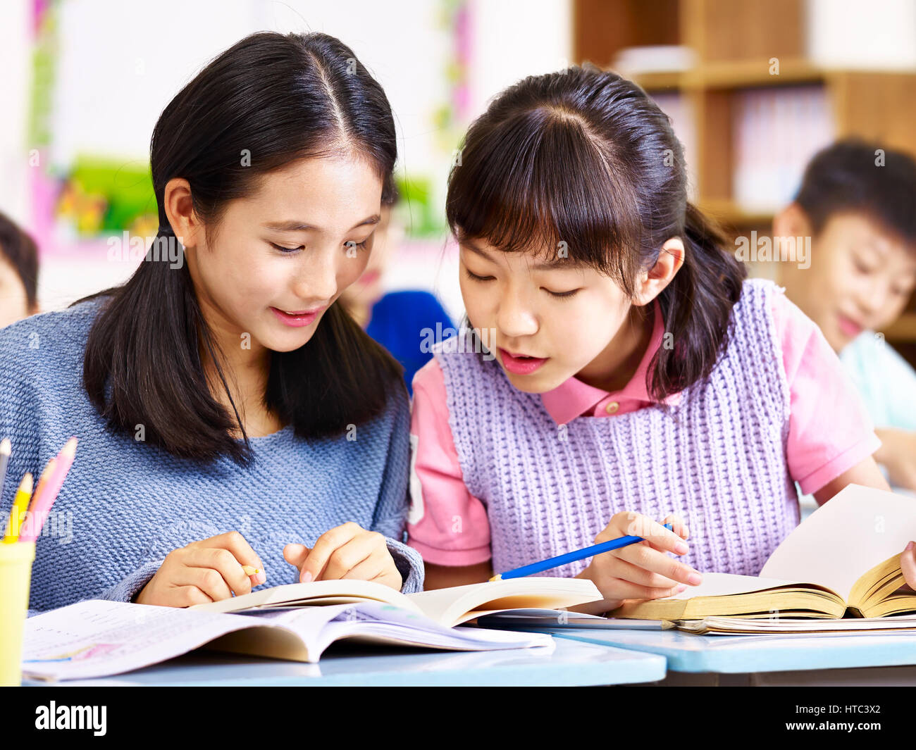 zwei asiatische elementare Schulmädchen Schreibtisch Kumpels haben einer Diskussion während des Unterrichts im Klassenzimmer. Stockfoto