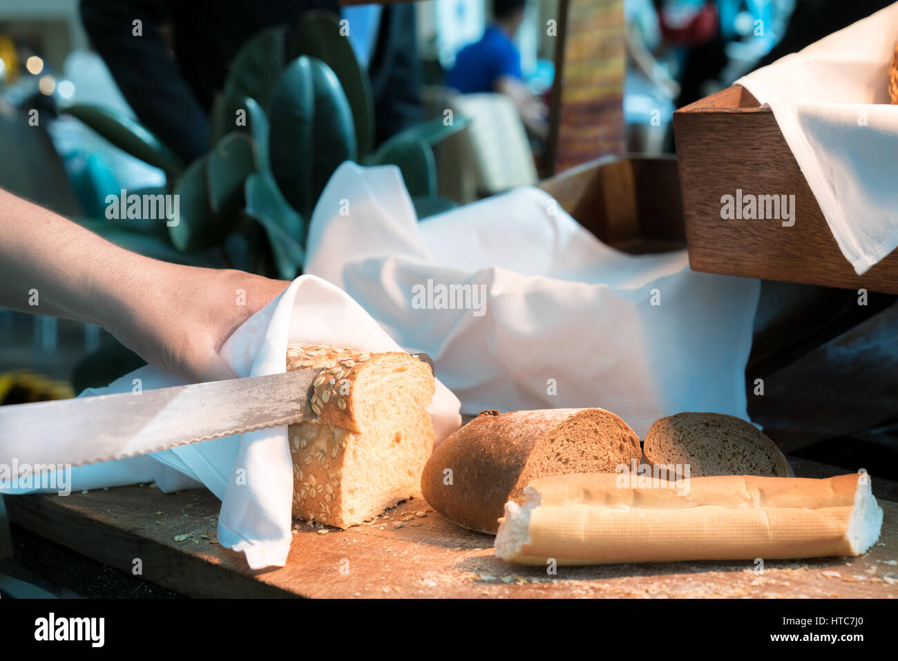 Männlich Hände schneiden wheaten Brot auf dem Holzbrett mit Frühstück im Hotel. selektiven Fokus Stockfoto