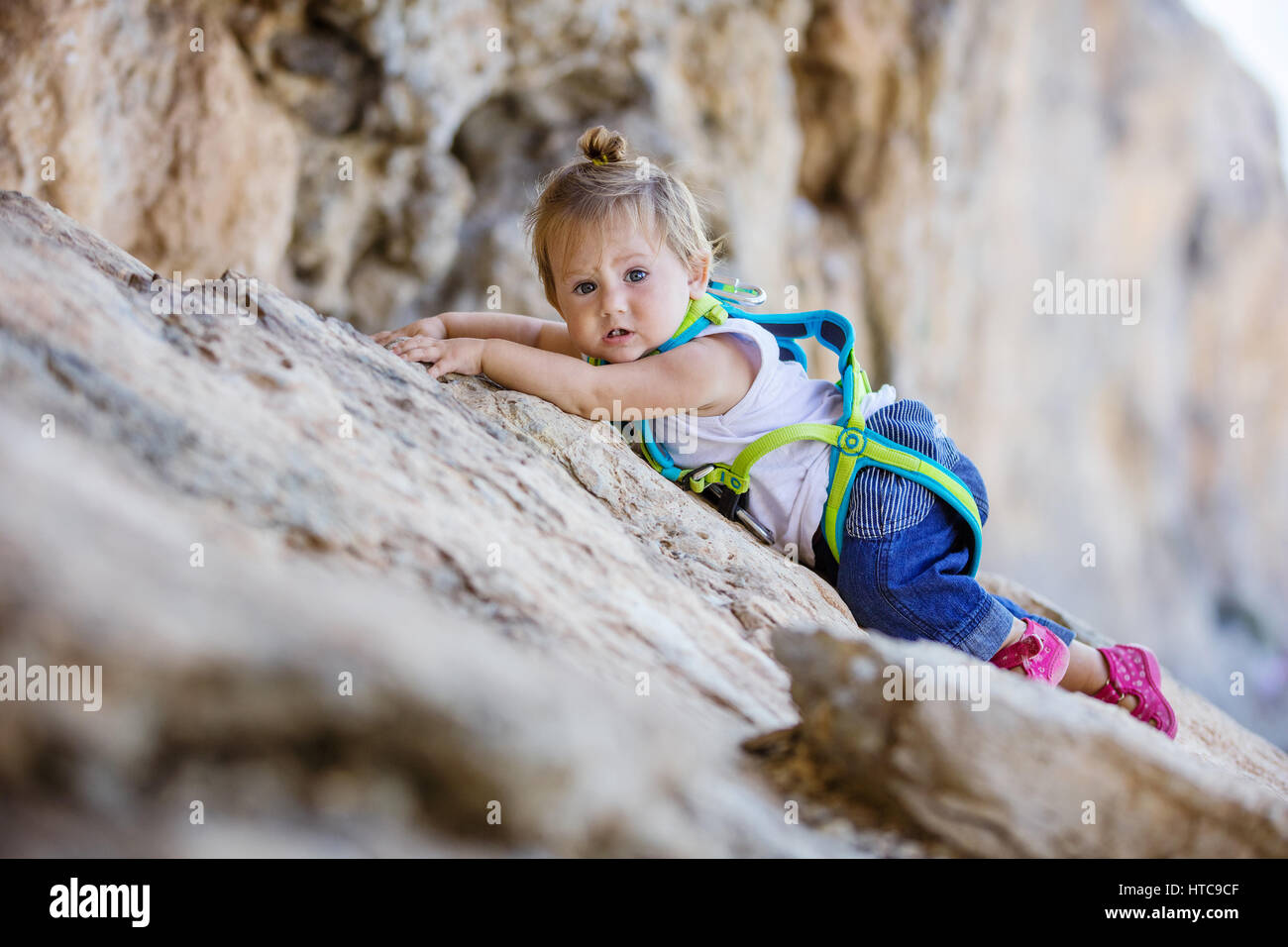 Kleines Mädchen in Sicherheitsgurt Klettern auf Felsen Stockfoto