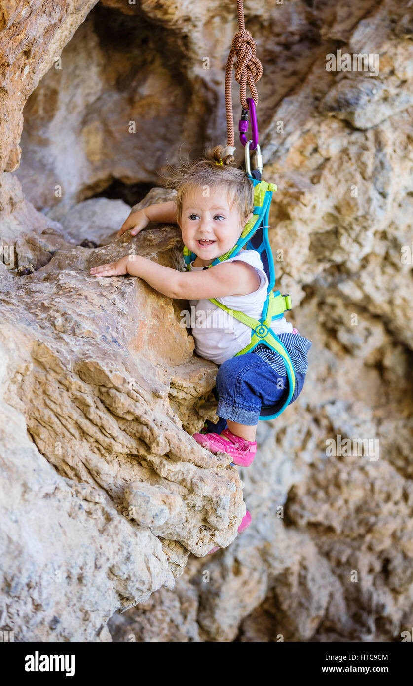 Glückliche kleine Mädchen in Sicherheitsgurt Klettern auf Felsen Stockfoto
