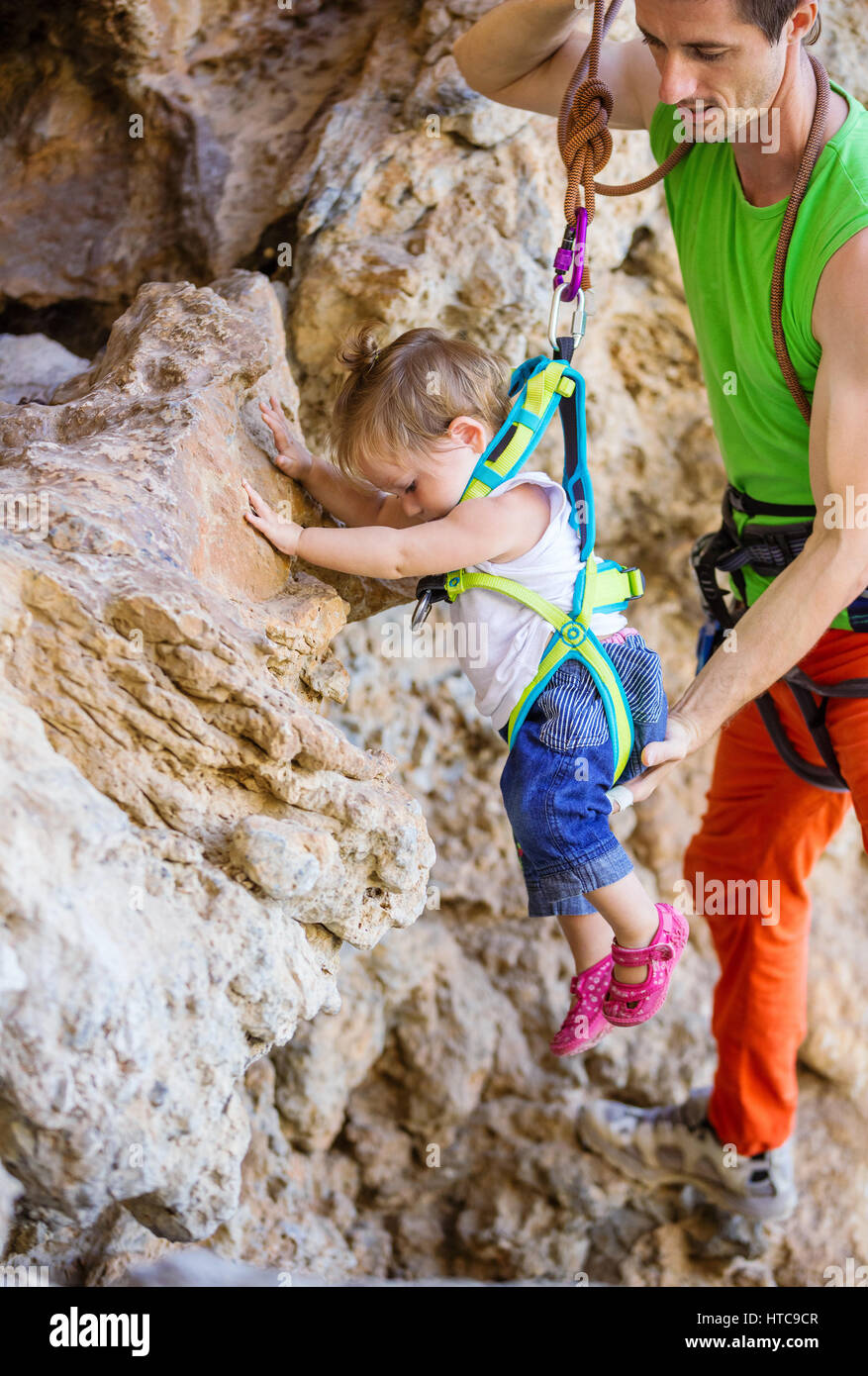 Kletterer, die helfen, seine kleine Tochter in Sicherheitsgurt auf Klippe zu halten Stockfoto