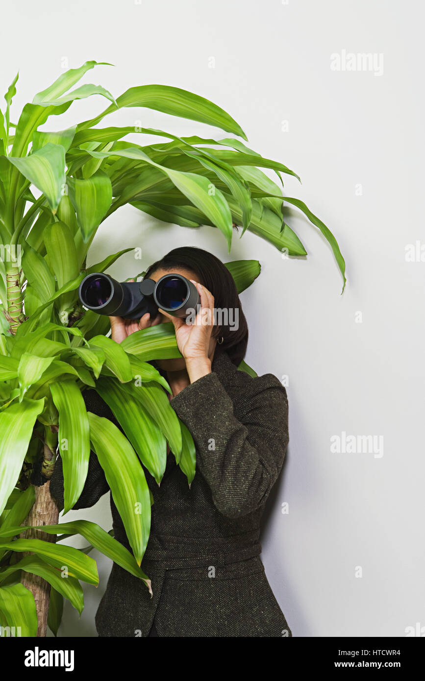 Geschäftsfrau, versteckt sich hinter der Pflanze mit dem Fernglas Stockfoto