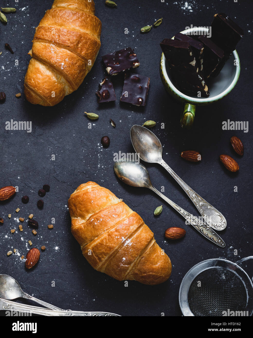 Frische Croissants, Schokolade, Gewürzen und Nüssen auf dunkle Tafel Hintergrund. Essen-Stilleben. Ansicht von oben Stockfoto