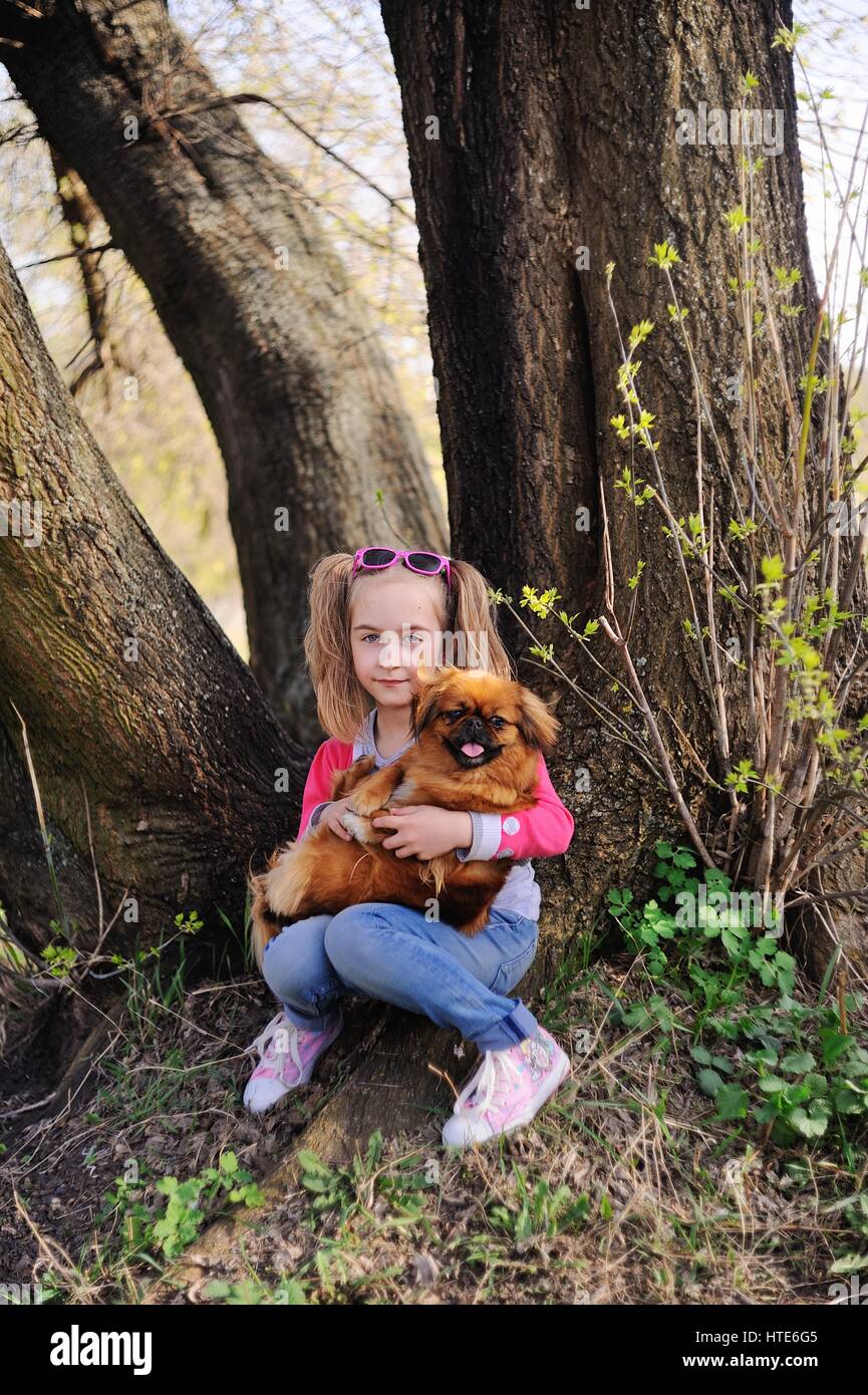 Babymädchen mit ein Pekinese sitzen auf dem Rasen unter einem großen