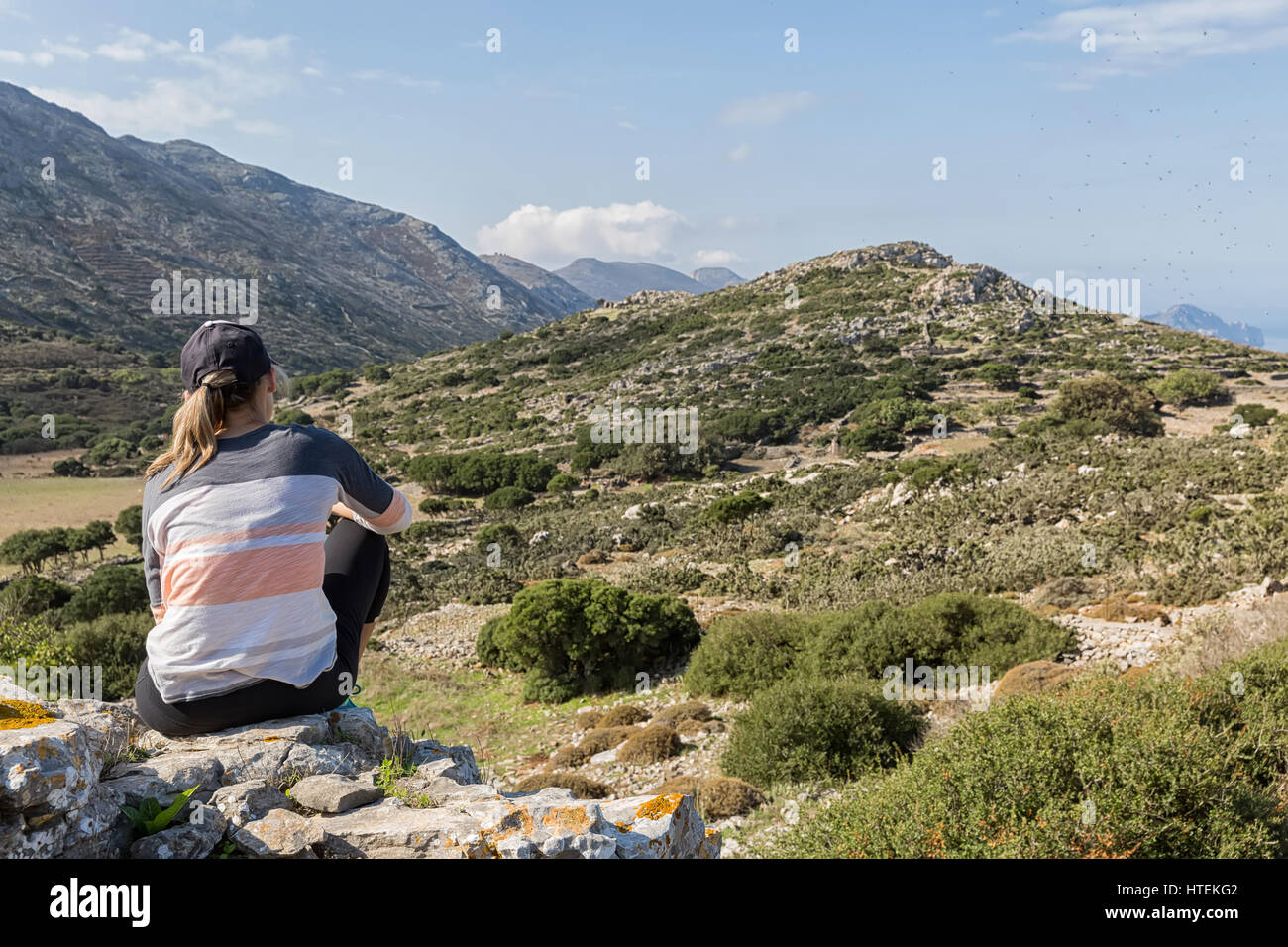 Frau sitzt auf Felsen Essen einen Snack und bewundern Sie die wunderschöne Landschaft Blick auf die grünen Berge, Amorgos Island, Griechenland Stockfoto