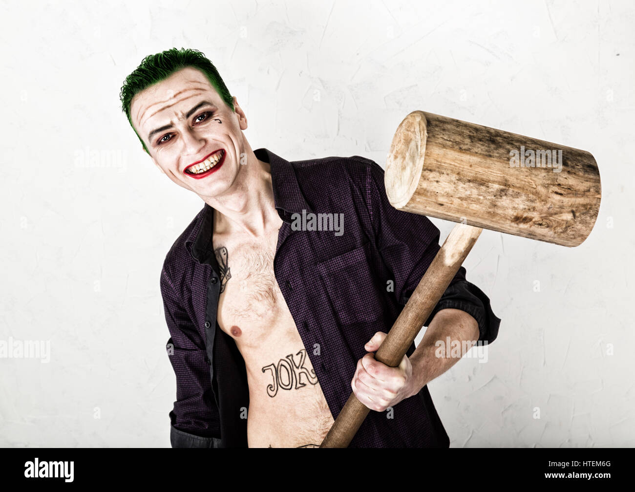 Kerl mit verrückten Joker Gesicht, grüne Haare und idiotische Lächeln. Karneval Kostüm. halten Hammer für Cricket. Stockfoto
