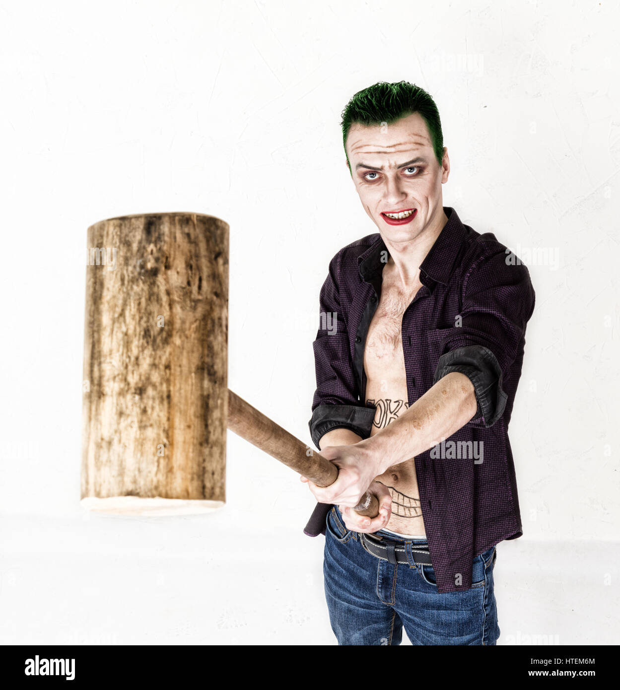 Kerl mit verrückten Joker Gesicht, grüne Haare und idiotische Lächeln. Karneval Kostüm. halten Hammer für Cricket. Stockfoto