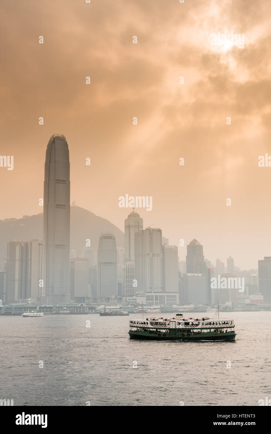 Mit der Fähre in den Victoria Harbour mit den Wolkenkratzern und die Skyline von Hong Kong, mit der Sonne durch dramatische Wolken. China. Stockfoto