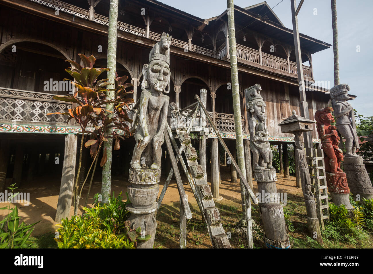 Patong oder Holz geschnitzte Bildnisse stehen neben einem Lamin oder Langhaus Eingang mit Holz geschnitzten Schritten erstellt aus einem einzigen Stück Bornean Ironwood (Kayu Stockfoto