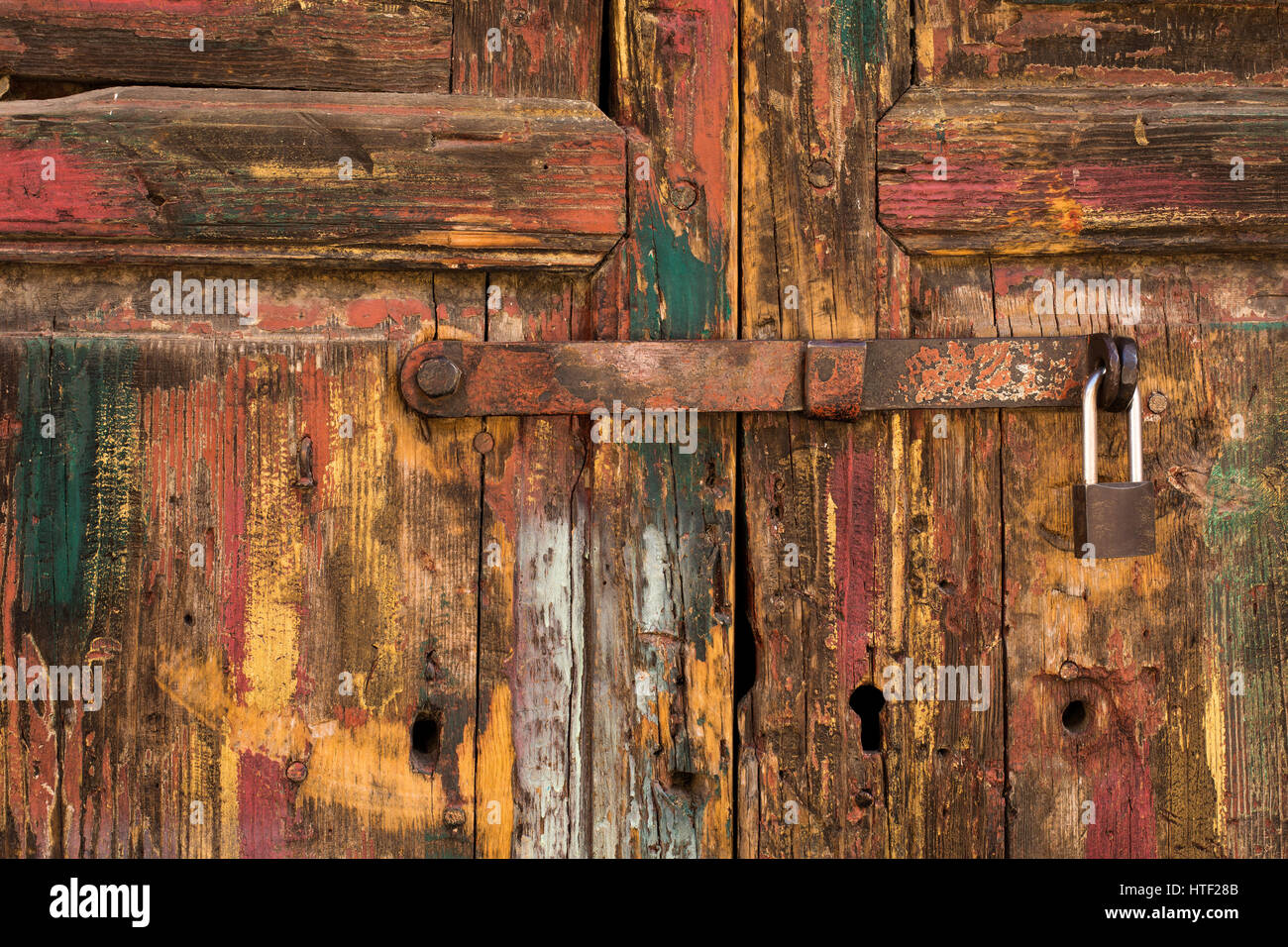 Rustikale Holztür mit Vorhängeschloss und Hauch von grünen, roten, gelben und weißen Farbe Stockfoto