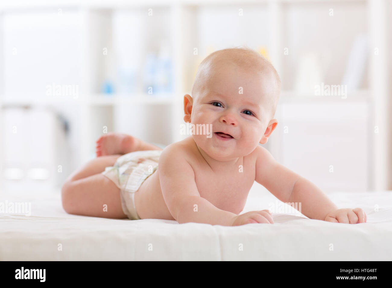 Niedliche Baby Säugling Junge tragen Windel im Bett liegend in weißem Licht Schlafzimmer oder Kinderzimmer. Textil- und Bettwäsche für Kinder. Stockfoto