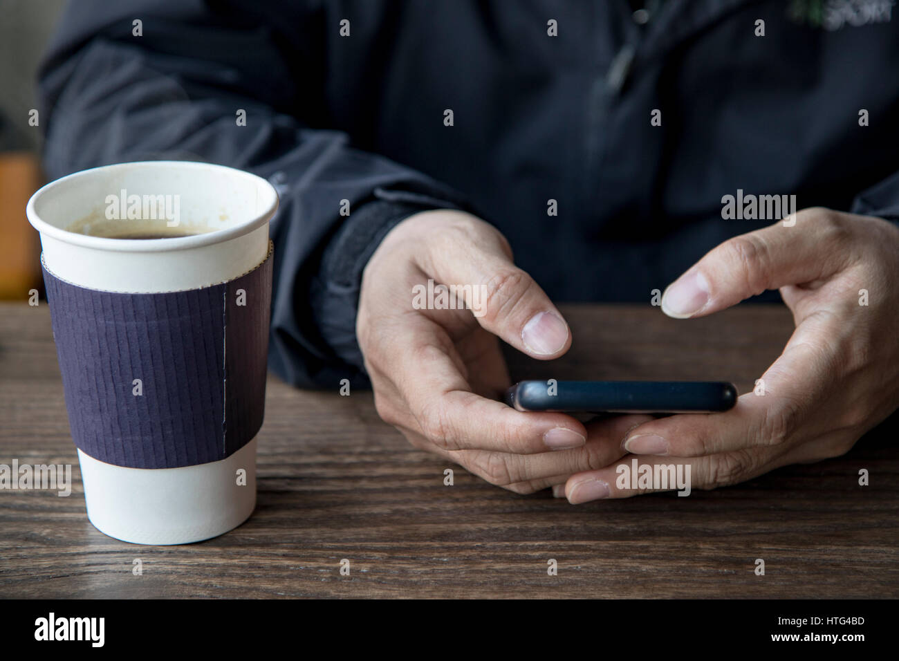 ein Mann nutzt das Smartphone auf dem Tisch neben einer Tasse Kaffee Stockfoto