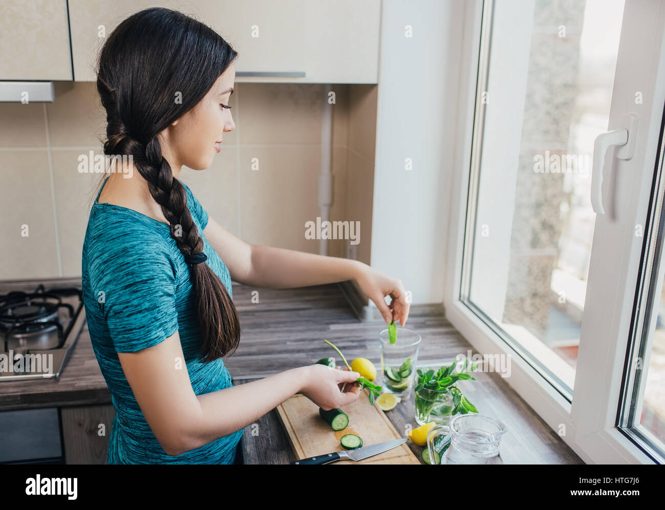 glückliche junge Frau machen, Wasser mit Gurke, Minze und Zitrone in der Küche zu Hause zu entgiften. Gesundes Getränk. Gewicht-Verlust-Diät Konzept. Prozess der Vorbereitung e Stockfoto