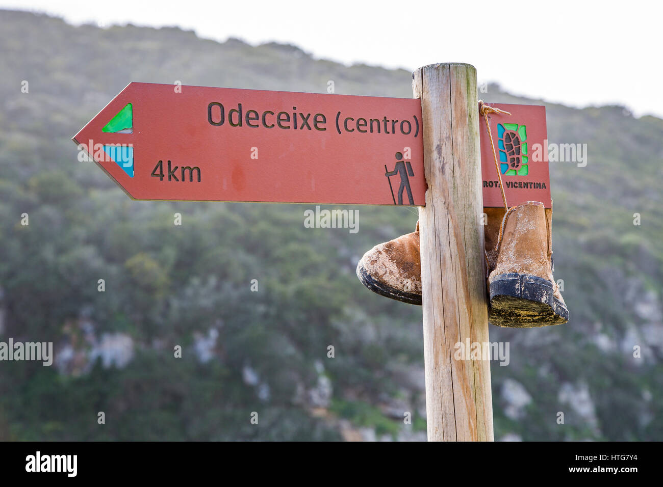 Wegweiser für Odeceixe, entlang der Rota Vicentina Weitwanderweg in der Algarve in Portugal, mit Wanderschuhen zum Trocknen gehängt. Stockfoto