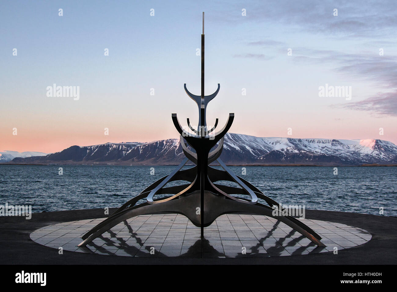 Symmetrische Ansicht von The Sun Voyager Skulptur in Reykjavik, Island gegen Berge bei Sonnenuntergang Stockfoto