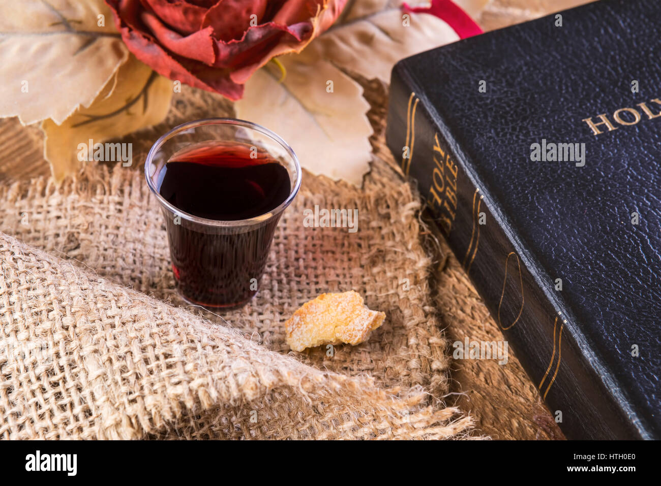 Die Kommunion. Tasse aus Glas mit Rotwein, Brot und Bibel auf Holztisch Nahaufnahme. Fokus auf Glas Stockfoto
