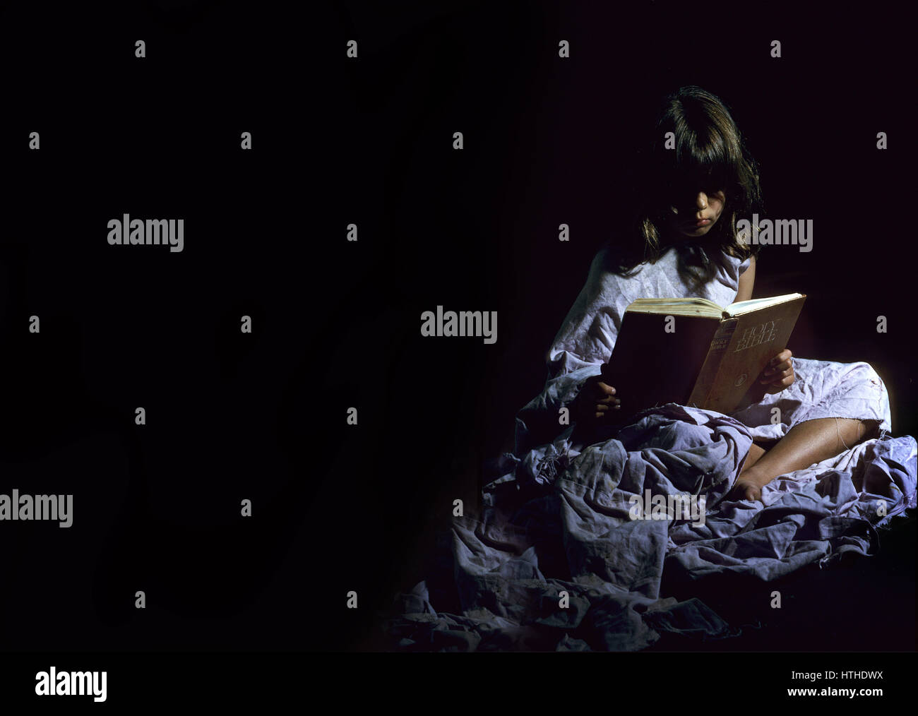 Ein kleines Mädchen sitzt in einem dunklen Raum, die Bibel zu lesen Stockfoto