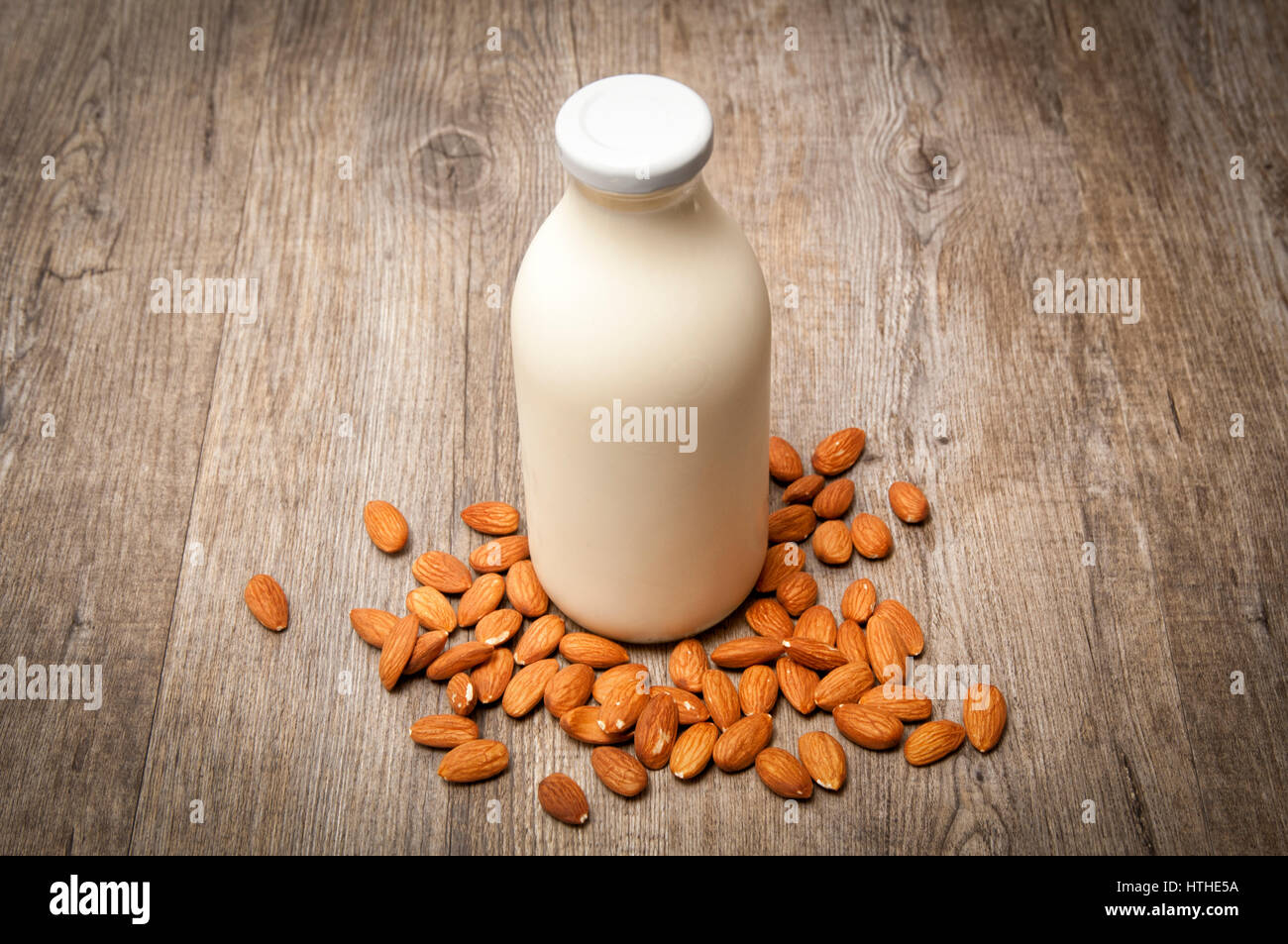 Milchflasche mit Mandelmilch und ganzen Mandeln auf einem Holztisch Stockfoto