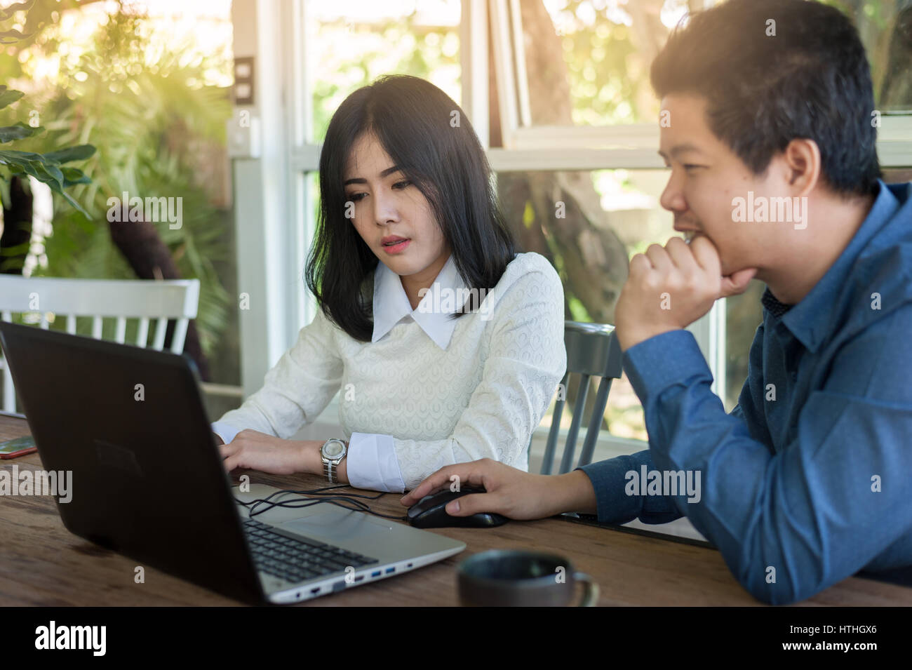 Junge asiatische Geschäftsmann und Geschäftsfrau sprechen über ihre Arbeit beim Laptop-Monitor im Café betrachten. Startup-Unternehmen für freie Arbeiten Stockfoto