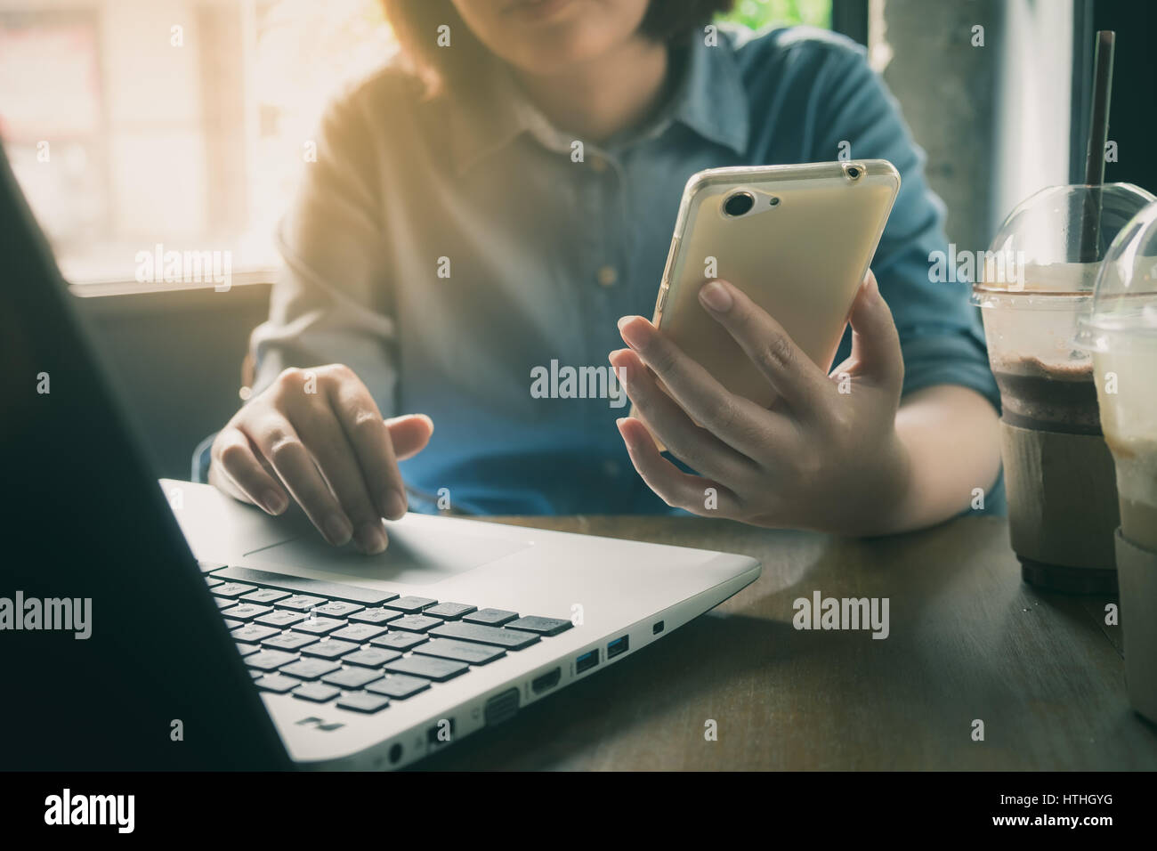 Frau Hand Holdong Smartphone während der Arbeit mit Laptop im Café. Freier Mitarbeiter am Werktag mit Online-Business-Konzept mit Jahrgang Stockfoto
