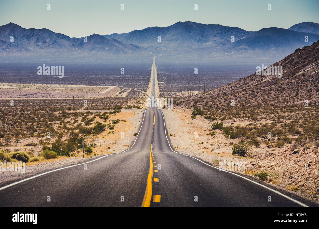 Klassische Panoramablick auf eine endlose geraden Straße läuft durch die karge Landschaft des amerikanischen Südwestens mit extremer Hitze Dunst auf eine schöne h Stockfoto