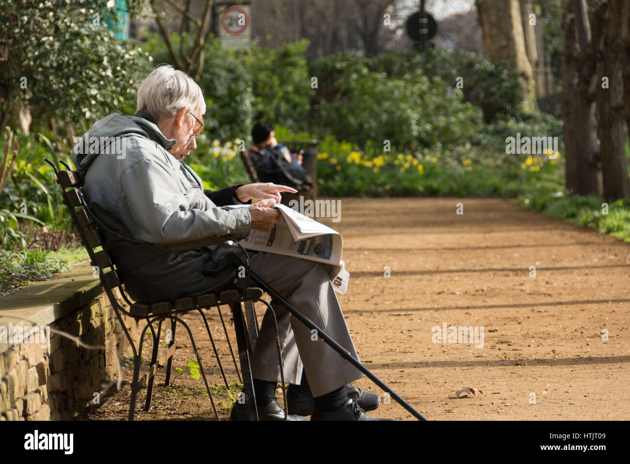 Ein Alter Mann sitzt auf einer Parkbank, lesen eine Zeitung, in der Frühlingssonne am Gordon Square, London, UK Stockfoto