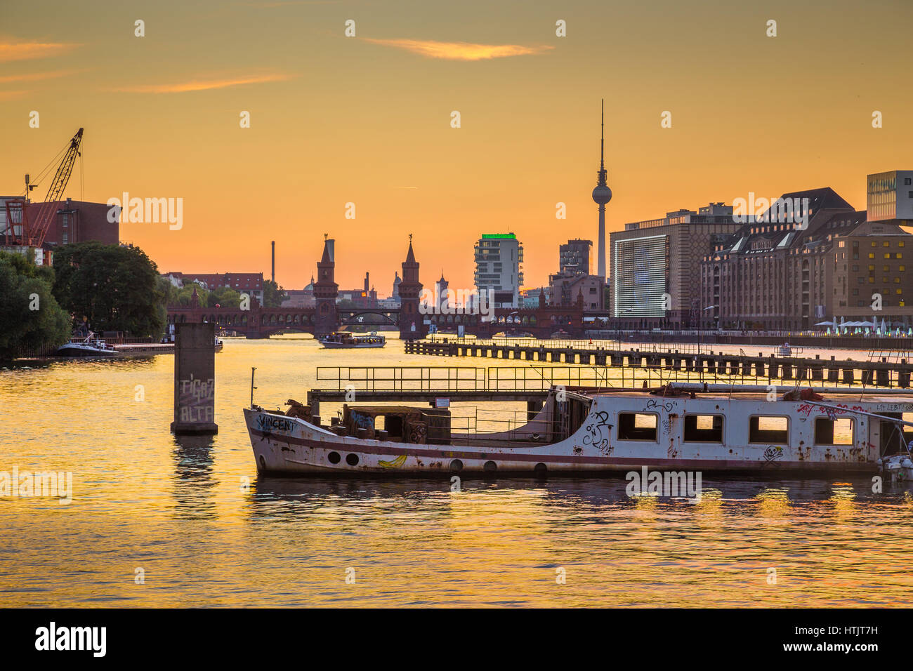 Berliner Skyline mit berühmten Fernsehturm und Oberbaumbrücke mit alten Schiffswrack liegen im Fluss Spree in schönen goldenen Abendlicht bei Sonnenuntergang im Sommer Stockfoto