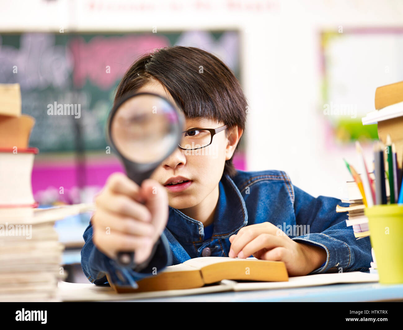 neugierig asiatische Schüler eine Lupe vor ein Auge halten. Stockfoto