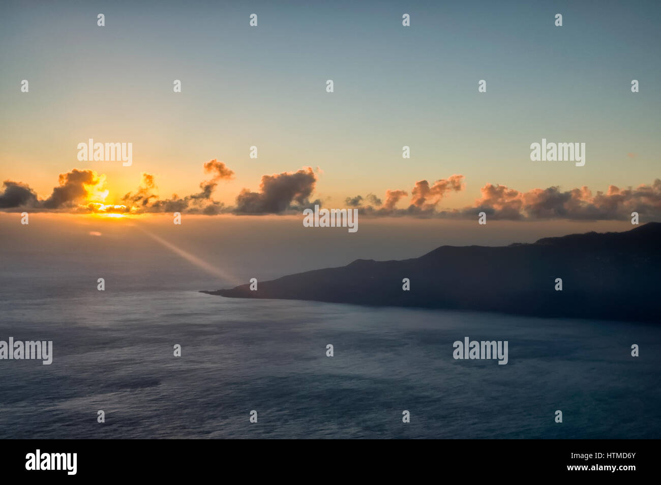 Küste. La Palma. Luftaufnahme von La Palma, die Sonne scheint durch niedrige Wolken kurz vor Sonnenuntergang. Ein Lichtstrahl trifft auf die Küste. Einen klaren, blauen Himmel über dem cloudscape Kulisse während ruhige See, im Vordergrund. Stockfoto
