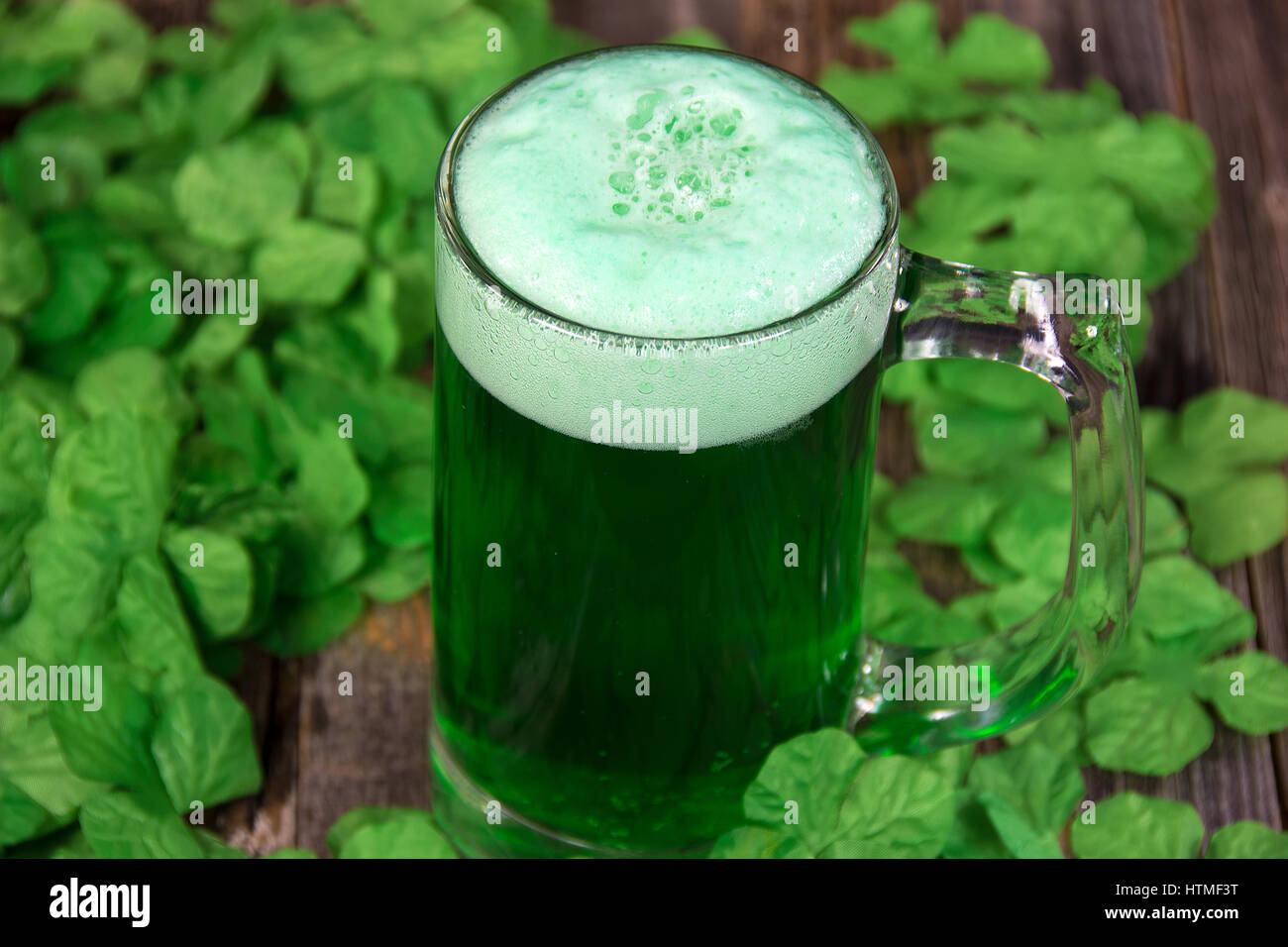 schaumige grünes Bier im Becher mit irischen Kleeblätter auf Holz Stockfoto