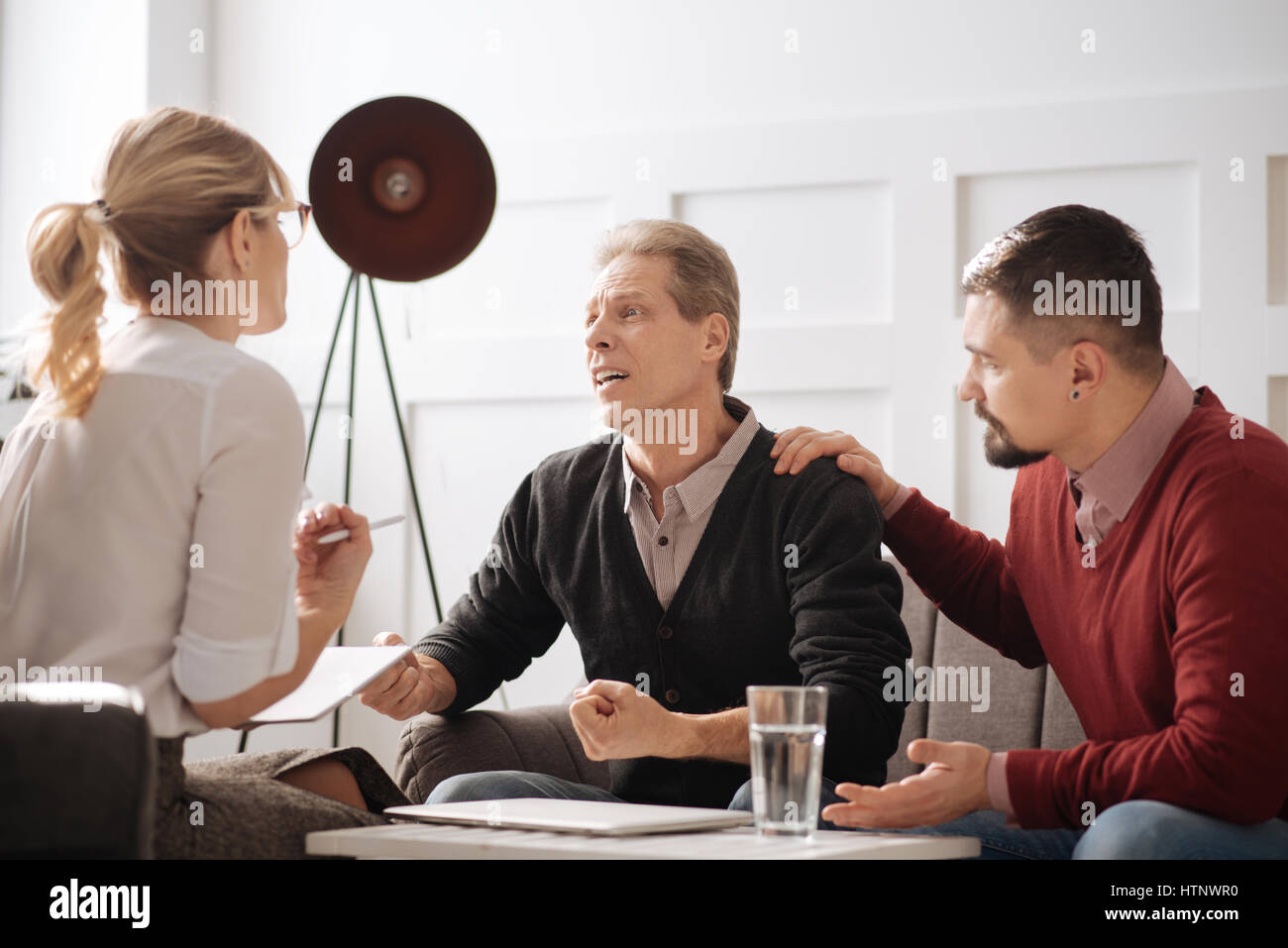 Persönliche Probleme. Emotionale unglücklich netter Mann ballte die Fäuste und betrachten der Psychologe bei dem Versuch, seine Emotionen zu bewältigen Stockfoto