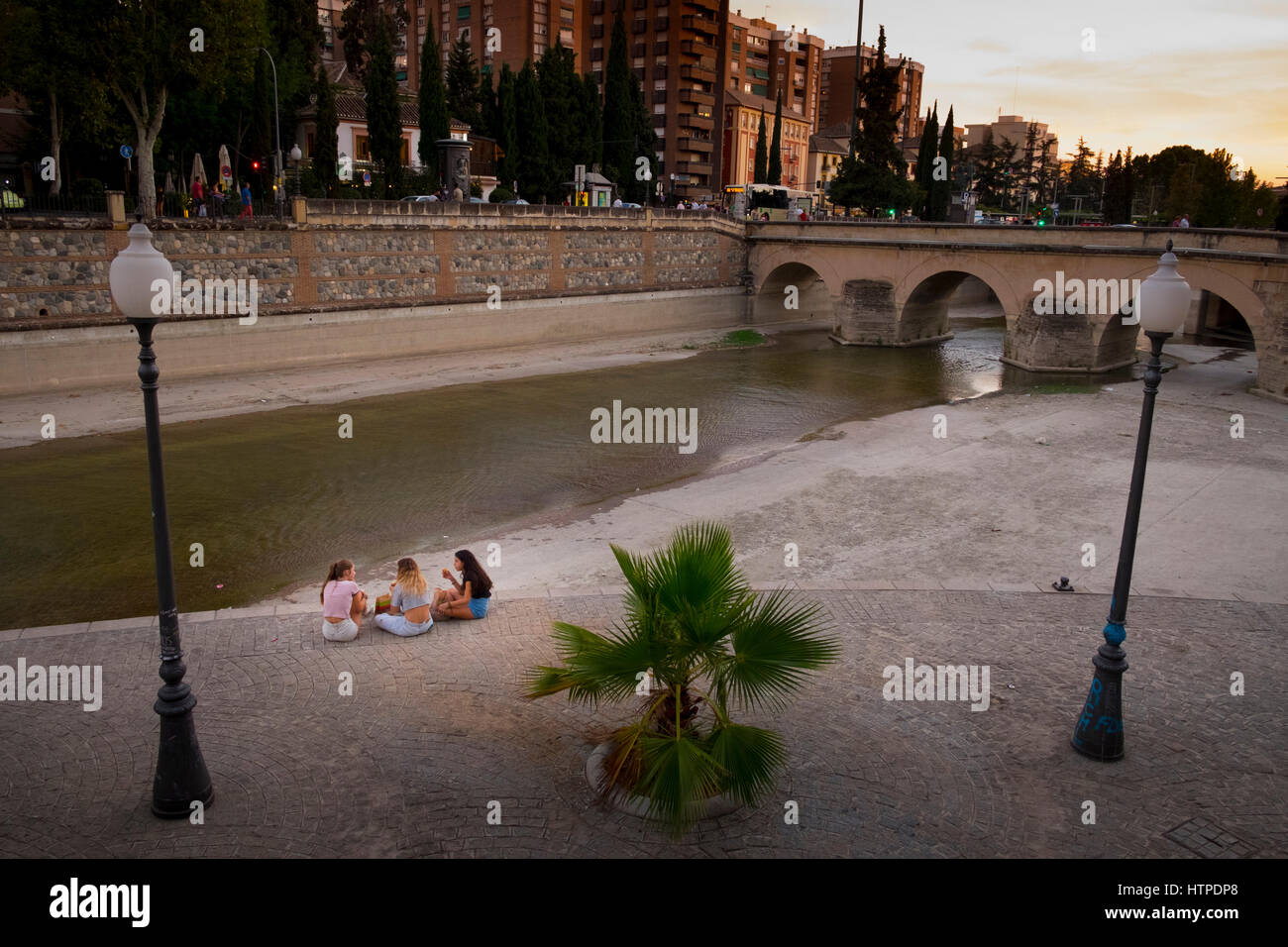 Drei junge Mädchen zurück zu Kamera sitzen und reden vom Fluss Genil und Puente Arabe Brücke in Granada am Ende des Tages Stockfoto