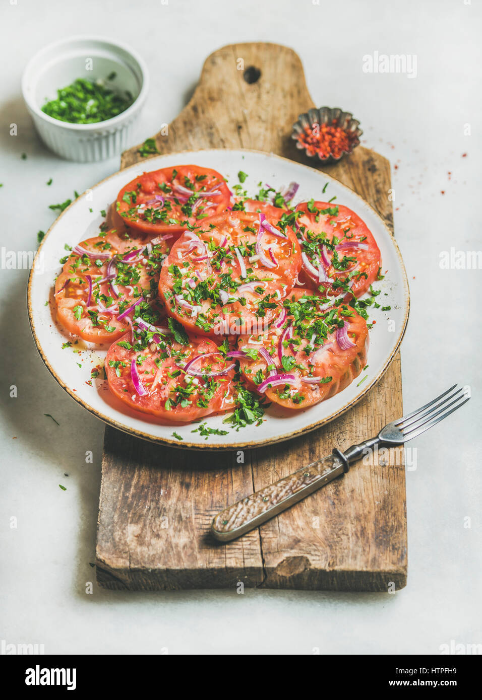 Frische Heirloom Tomaten, Petersilie und Zwiebel Salat in weißer Teller auf rustikalem Holzbrett über hellen grauen Marmor Hintergrund, selektiven Fokus. Sauber, Essen, Stockfoto