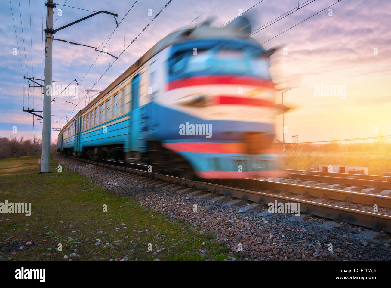 High-Speed elektrische Passagierzug in Bewegung auf Eisenbahn bei Sonnenuntergang. Verschwommene alten s-Bahn. Bahnhof gegen blauen Himmel. Eisenbahn Reisen, ra Stockfoto