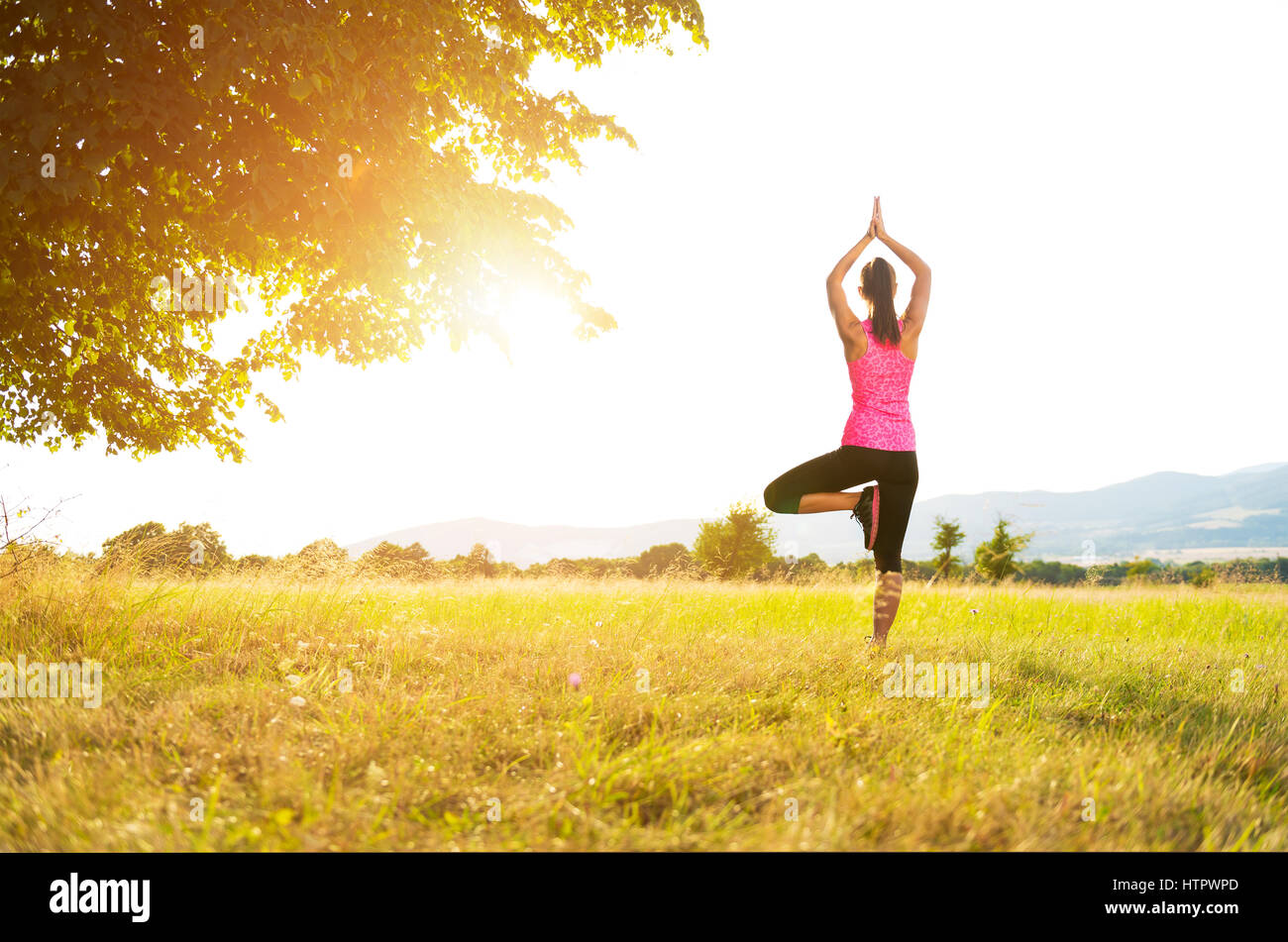 Junge athletische Frau Yoga auf einer Wiese bei Sonnenuntergang, Bild mit Lens flare Stockfoto