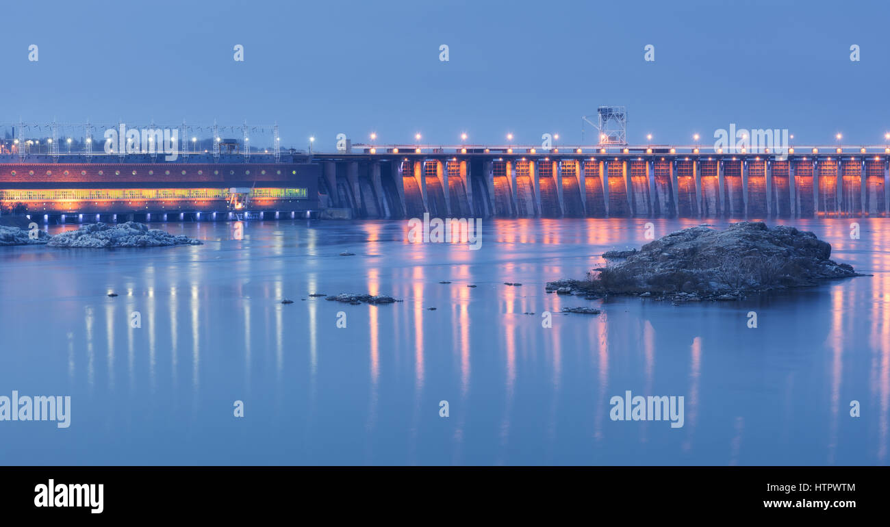 Dam in der Nacht. Schöne Industrielandschaft mit Wasserkraftwerk Damm, Brücke, Fluss, Stadt Beleuchtung spiegelt sich im Wasser, Felsen und Himmel. Stockfoto