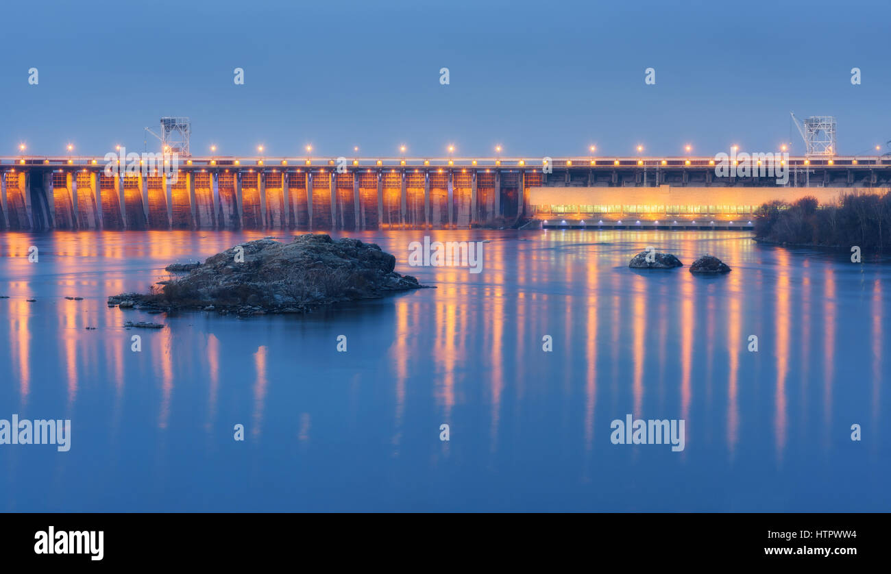 Dam in der Nacht. Schöne Industrielandschaft mit Wasserkraftwerk Damm, Brücke, Fluss, Stadt Beleuchtung spiegelt sich im Wasser, Felsen und Himmel. Stockfoto