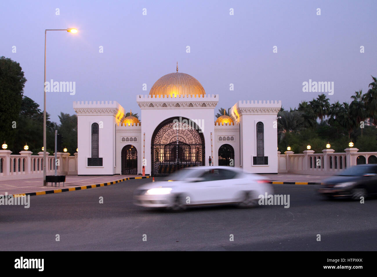 Autos fahren vorbei an der Einfahrt zum Al Qudaibiya Palast im Abendlicht, in Gudaibiya Bezirk von Manama, Bahrain. Stockfoto