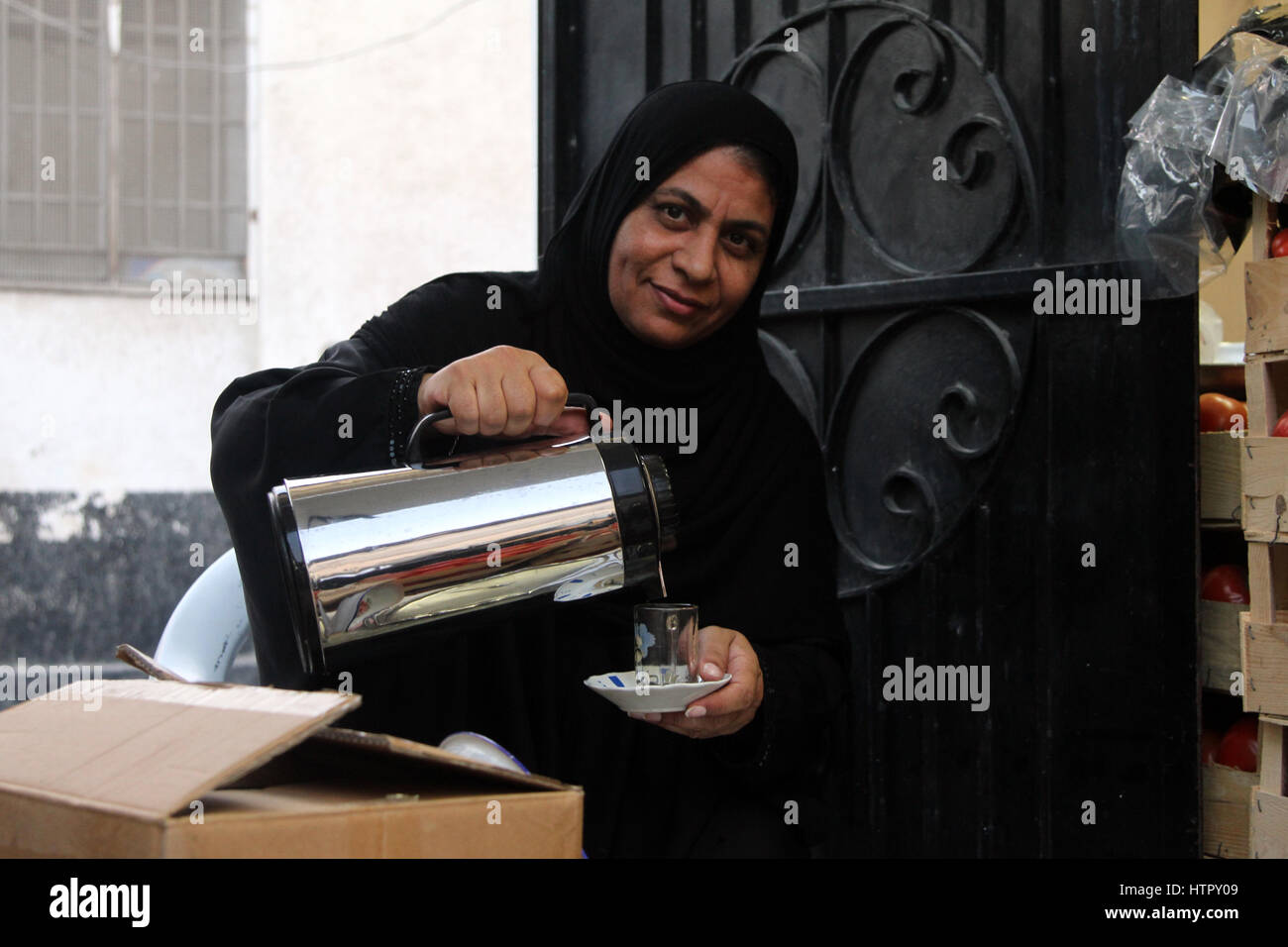 Bahrains schiitischen Trägerin die traditionelle schwarze Abaya, ergießt sich eine Tasse Tee. Stockfoto