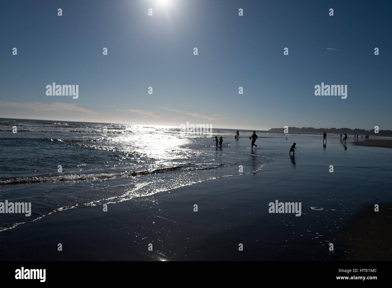 Stinson Beach, California, Vereinigte Staaten von Amerika - 12. März 2017: Sonnenlicht beleuchtet das Wasser als Badegäste spielen in den Wellen in Stinson Beach, Kalifornien, Stockfoto